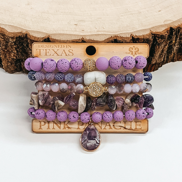 purple bracelet set that comes in different sizes and shades, it includes gold beads, a white marbled bead, a purple crystal beaded bracelet, and a purple crystal charm in a teardrop shape