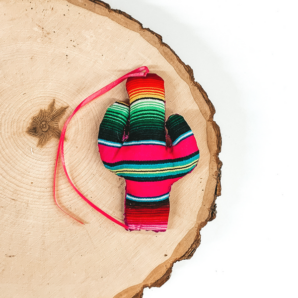 Cactus shaped freshie that is serape print with pink string. This is laying on a piece of wood that is on a white background.