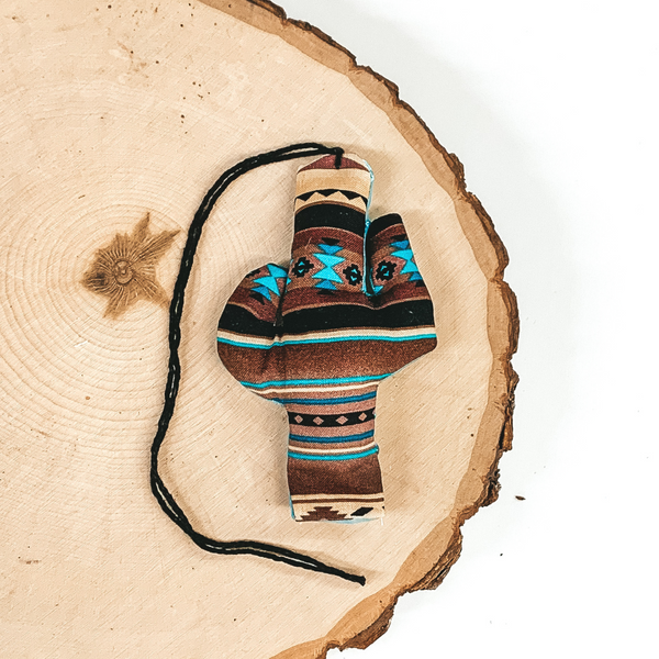 Cactus shaped freshie that is brown and turquoise aztec print with black string. This is laying on a piece of wood that is on a white background.