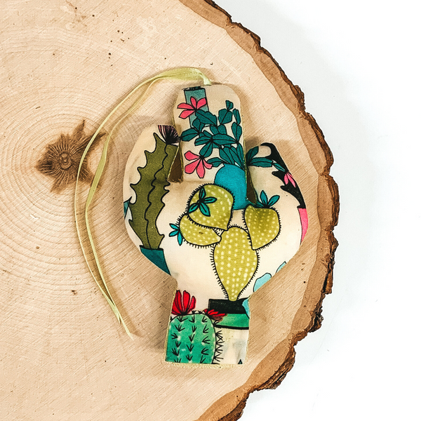 Cactus shaped freshie that is a colorful succulent print with light yellow string. This is laying on a piece of wood that is on a white background.
