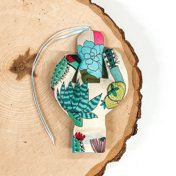 Cactus shaped freshie that is a colorful succulent print with light blue string. This is laying on a piece of wood that is on a white background.