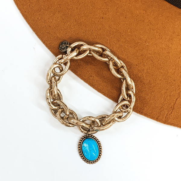Thick matte gold chain link bracelet. This bracelet has a tiny oval turquoise cabochon stone. This bracelet is pictured on a white and camel background. 