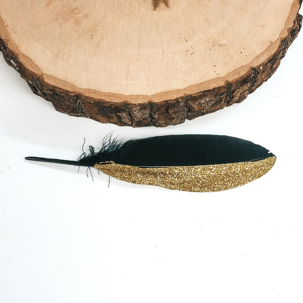 This feather is half black and half glitter gold. This feather is pictured on a white background. 