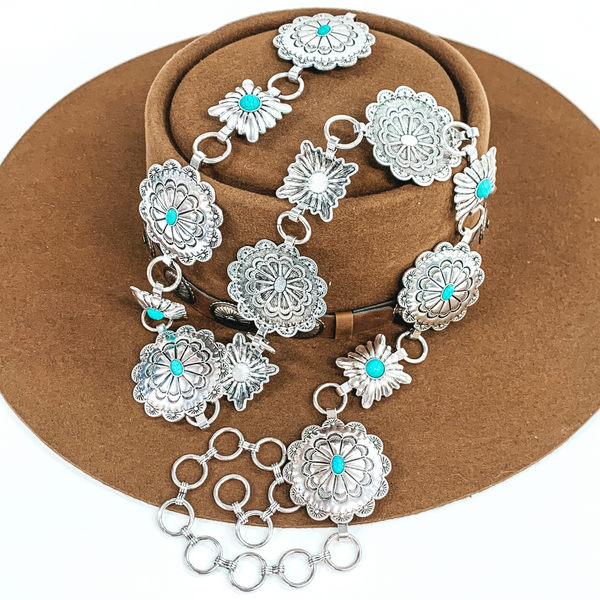 Circle and square silver concho belts with tiny center turquoise stones. This belt includes circle loops to make it adjustable. This belt is pictured laying on a brown hat on a white background.