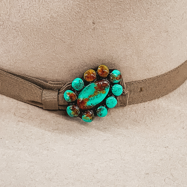 This hat pin is a short, oval concho. The main color is turquoise and is mixed with brown, red and yellow like real turquoise. This hat pin is pictured in front of a beige hat band.