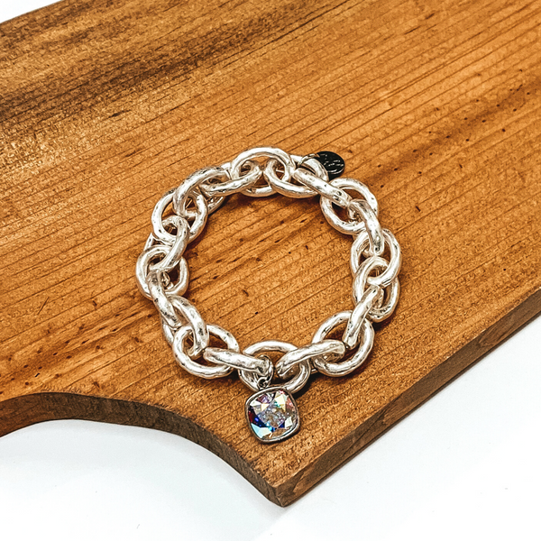 Worn silver chunky chained bracelet. This bracelet has a AB cushion cut crystal. This bracelet is pictured on a piece of wood on a white background. 