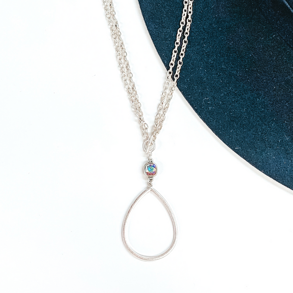 Double layered silver chained necklace with front, small toggle clasp. This necklace includes a hanging AB cushion cut crystal and an open teardrop silver pendant. This necklace is pictured on a navy and white background.