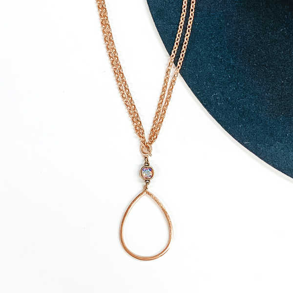 Double layered gold chained necklace with front, small toggle clasp. This necklace includes a hanging AB cushion cut crystal and an open teardrop silver pendant. This necklace is pictured on a navy and white background.