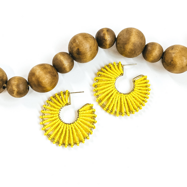 Gold outlined, thick hoops. Wrapped around the gold outline are a lemon yellow beaded string. These earrings are pictured on a white background with dark brown beads at the top of the picture. 