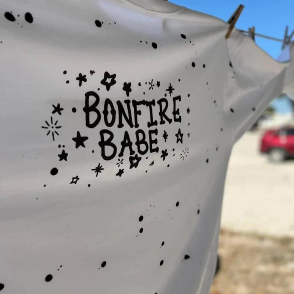 White sweatshirt on a clothing line with black paint splatter and the words bonfire babe.