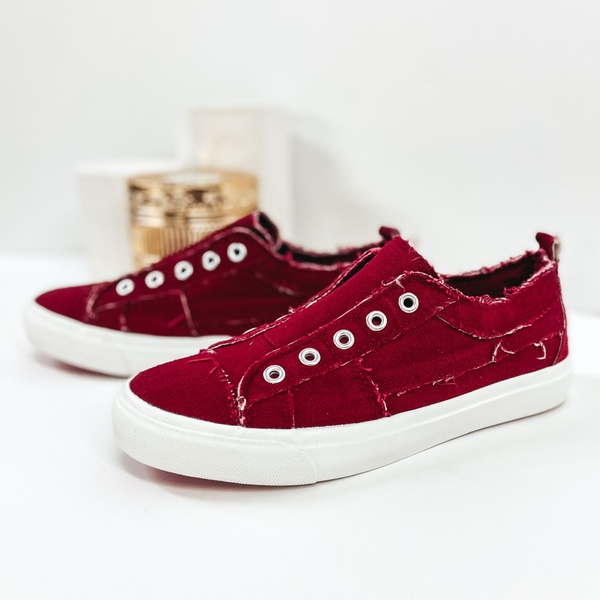 Maroon sneakers without laces and white soles. Pictured on white background.