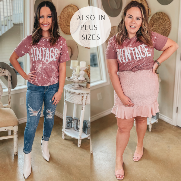 Two models wearing a dusty pink graphic tee with bleach splatters all over it and text in capital letters that says vintage. The model to the left is wearing the tee with ripped jeans and white ankle boots. The model to the right is plus size and wearing the tee with a light pink ruched skirt with a ruffle hem and nude strappy heels.