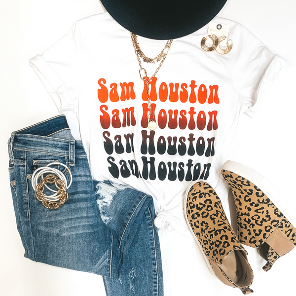 A white tee shirt with short sleeves and a crew neckline with an orange and black graphic that says "Sam Houston" in 4 rows. This tee is pictured on a white background with gold jewelry, leopard print sneakers, and distressed jeans.