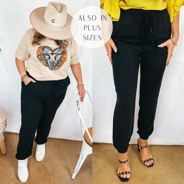 Models are wearing a pair of black drawstring joggers. Size large model has it paired with a cream graphic tee, a cream hat, and white sneakers. Size Small model has it paired with black heels.