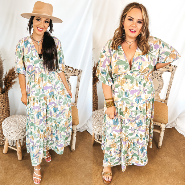 Models are wearing a green and purple pastel floral maxi dress. Size small model has it paired with white heels, a tan hat, and silver jewelry. Size large model has it paired with gold sandals and gold jewelry.