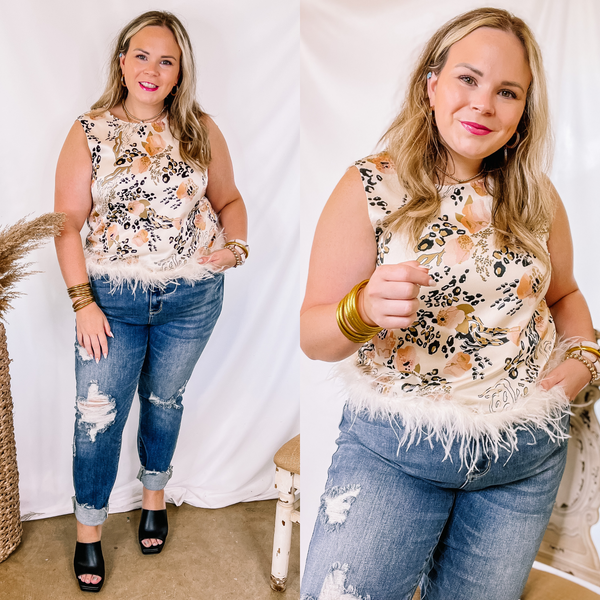 Model is wearing an ivory tank top with a mix animal print. This top is satin with a feather trim. Model has it paired with distressed skinny jeans, black heels, and gold jewelry.