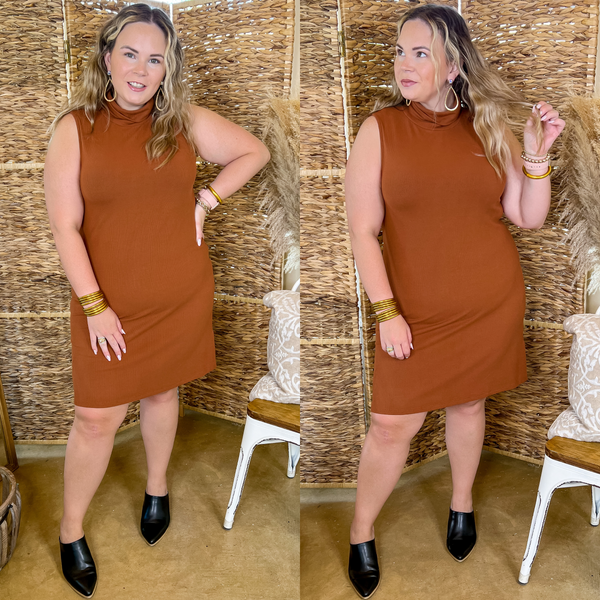 Model is wearing a rust orange short dress with tank top straps and a turtle neck. Model has this sweater dress paired with black mules and gold jewelry.