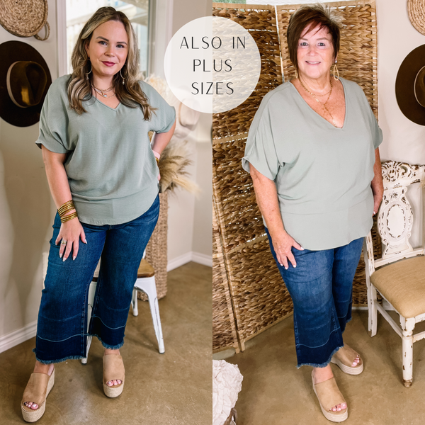 Model is wearing a sage green top with short sleeves and a v neck. Model has it paired with cropped wide leg jeans, tan wedges, and gold jewelry.