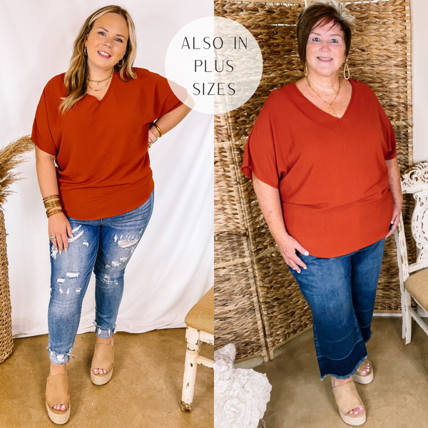 Model is wearing a rust red v neck top with short sleeves. Model has it paired with distressed skinny jeans, tan wedges, and gold jewelry.