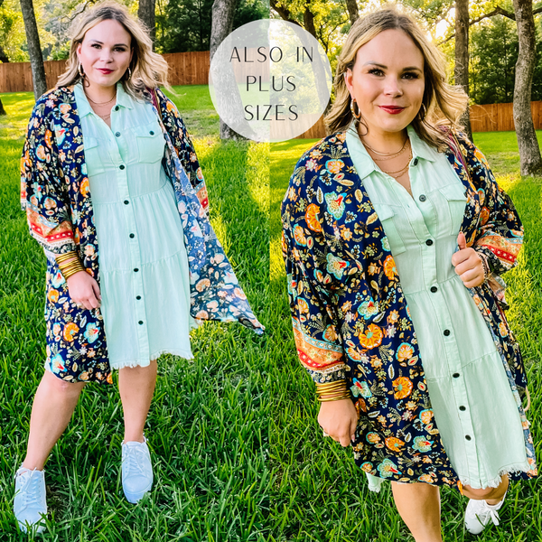Model is wearing a navy kimono with a gold floral print. Model has it on over a mint green dress with white sneakers and gold jewelry.