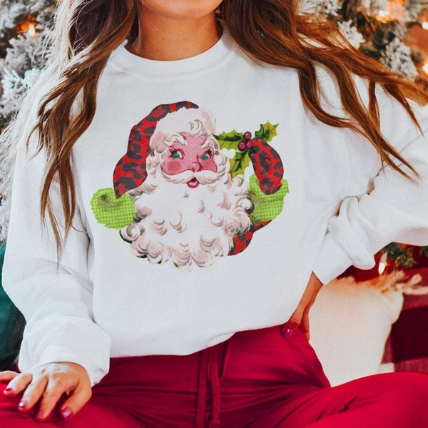 Model is sitting criss-cross with a white sweatshirt on. This sweatshirt has a picture of Santa Clause holding a mistletoe and wearing a red leopard hat and glove.