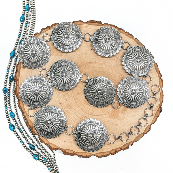 A silver circle concho belt placed on a wooden display on a white background with Navajo Pearls.