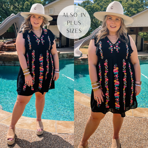 Model is wearing a black v neck dress with ruffle cap sleeves and colorful floral embroidery. Model has it paired with tan wedges, gold jewelry, and a beige hat.