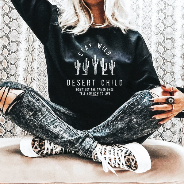 Model is wearing a black long sleeve sweatshirt with saguaro cactus. Model has it paired with black distressed skinnies and leopard sneakers.