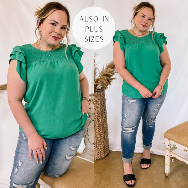 Model is wearing a green top with ruffle cap sleeves and a smocked upper. Model has it paired with cuffed boyfriend jeans, black heels, and gold jewelry.