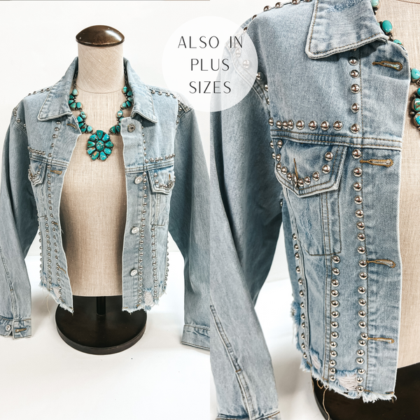A light wash denim jacket with silver studs and a distressed hemline. This long sleeve jacket is pictured on a mannequin with a large turquoise necklace.