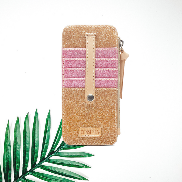 A gold glitter wallet with pink card holders and leather detailing. Pictured on a white background with a palm leaf.