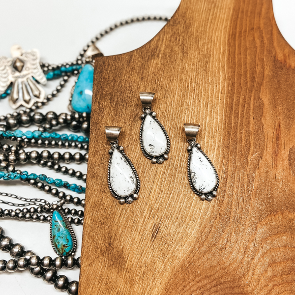 A genuine white buffalo pendant with a sterling silver outline and bail. Pictured on wooden background with navajo pearls and turquoise jewelry.