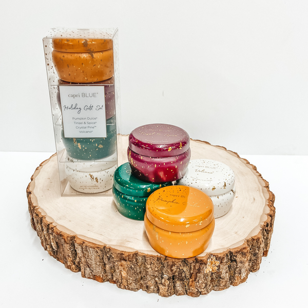 A set of 4 candles. One green, one white, one orange, and one maroon pictured next to a box containing the same candles. Candles are pictured on a wooden display on a white background.