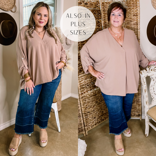 Model is wearing a taupe 3/4 sleeve top with a placket, and a flowy fit. Model has it paired with cropped denim jeans, tan wedges, and gold jewelry.