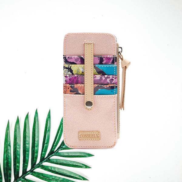 A pink glitter wallet with floral card slots and leather detailing. Pictured on a white background with a palm leaf.
