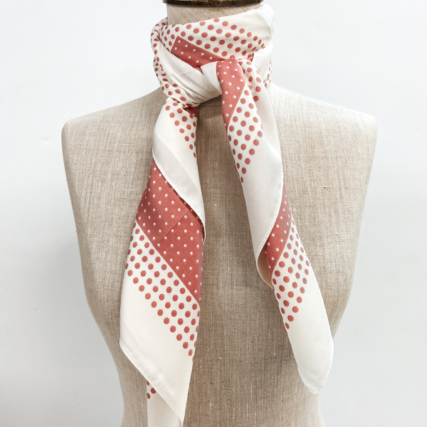 A pink and ivory polka dot scarf tied around the neck of a mannequin. Pictured on white background.