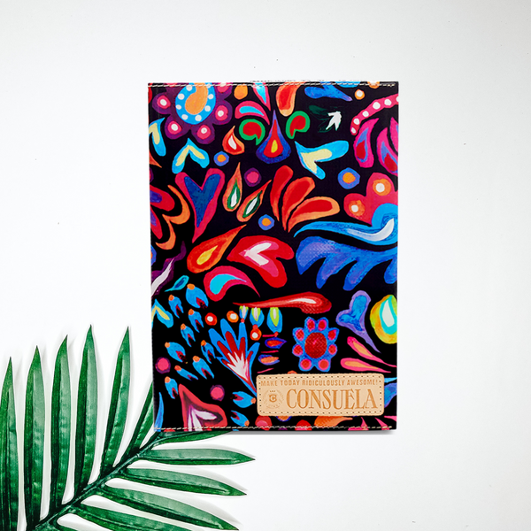 A black notebook cover with colorful paisley designs. pictured on white background with a palm leaf.