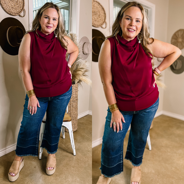 Model is wearing a maroon tank top with a high cowl neck. Model has it paired with cropped wide leg jeans, tan wedges, and gold jewelry.