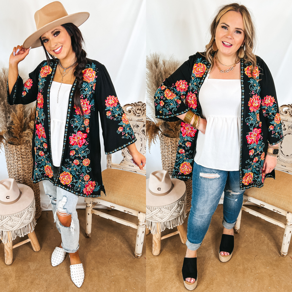 Models are wearing a black kimono with colorful floral embroidery. Both models have it on over a white babydoll tank top and distressed jeans. Size small model has it paired with white mules and a tan hat. Size large model has it paired with black wedges and gold jewelry.