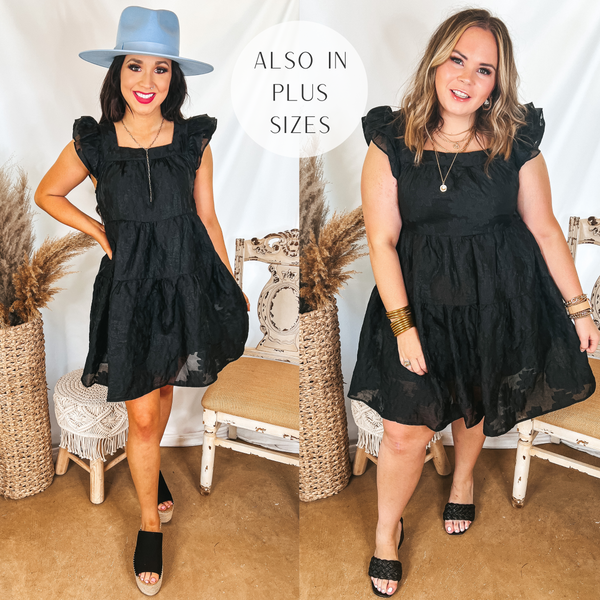 Models are wearing a black floral embossed dress with a tiered skirt and ruffle cap sleeves. Size small model has it paired with silver jewelry, a blue hat, and black wedges. Size large model has it paired with black heels and gold jewelry.