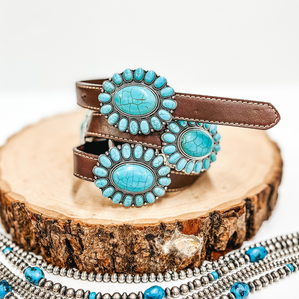 A brown belt with faux turquoise cluster conchos pictured on wooden display with Navajo pearls on a white background.