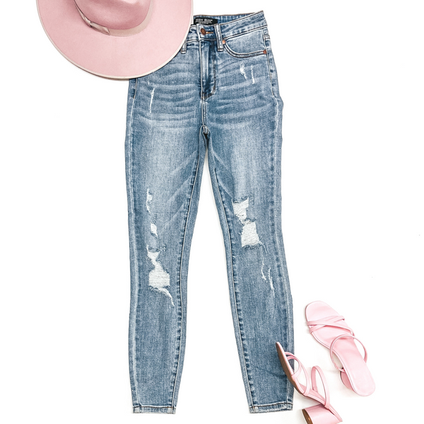 A pair of high waist skinny jeans with distressing on the legs. Pictured on a white background with a pink hat and pink strappy heels.