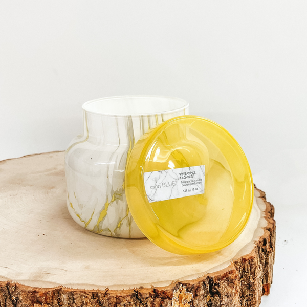 A yellow marble print jar candle pictured with the lid off. The candle is pictured on a white background with a wooden display.