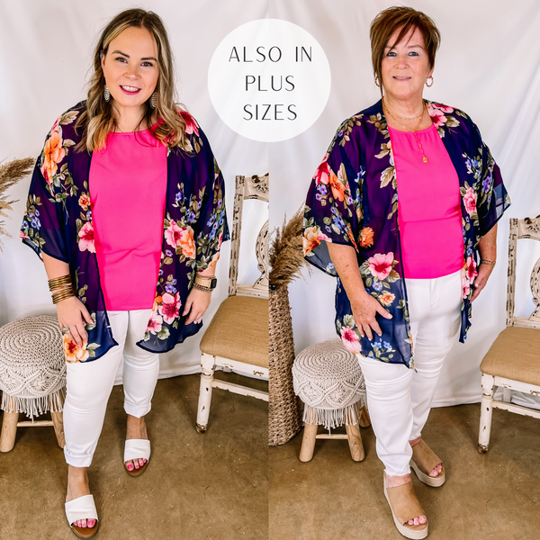 Models are wearing a navy blue floral kimono over a pink top and white skinny jeans. Size large model has it paired white sandals and gold jewelry. Plus size model has it paired with tan wedges and gold jewelry.