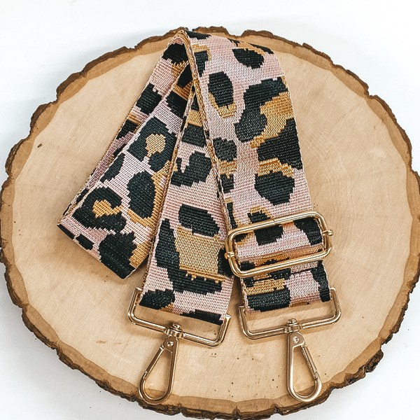 Shiny pink purse strap with a tan and black leopard print. This purse strap includes gold accents. This purse strap is pictured on a piece of wood on a white background. 
