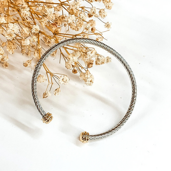 Silver cable bangle with gold cabochon ends. This bracelet is pictured on a white background with baby's breath on the top left corner. 
