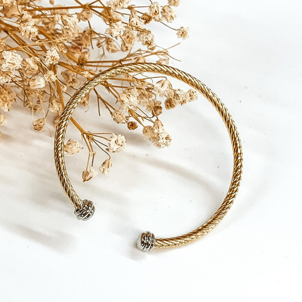 Gold cable bangle with silver cabochon ends. This bracelet is pictured on a white background with baby's breath on the top left corner. 