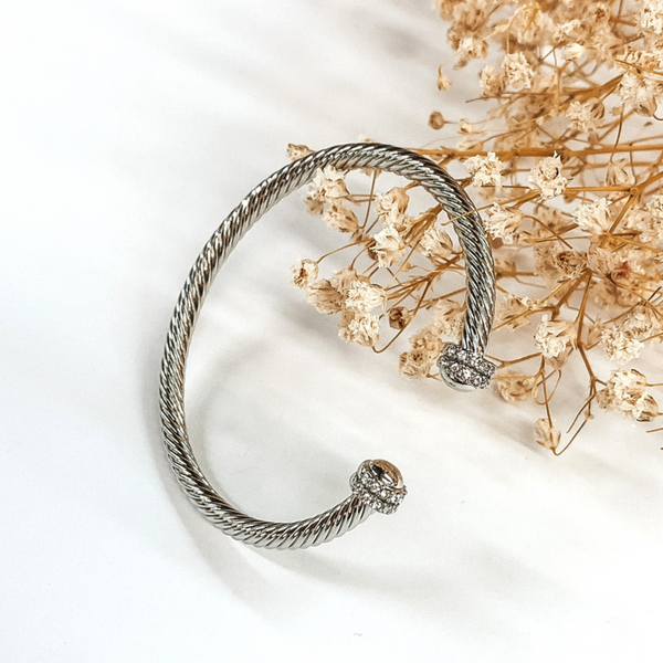 Silver cable bangle with clear crystal and silver cabochon ends. This bracelet is pictured on a white background with baby's breath on the top right corner. 