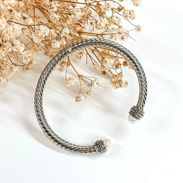 Silver cable bangle with white pearl and silver cabochon ends. This bracelet is pictured on a white background with baby's breath on the top left corner. 
