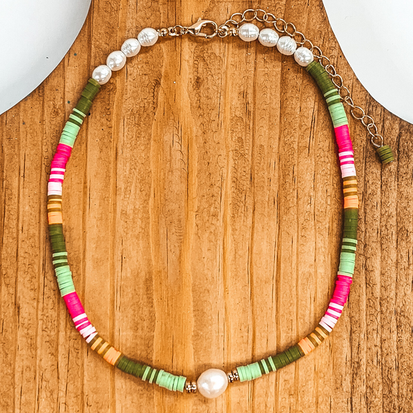 Thin rubber beads with a center white pearl and four pearls on either sides of the clasp. This necklace includes the colors green, light green, hot pink, light pink, and orange. This necklace is pictured on a brown block on a white background. 